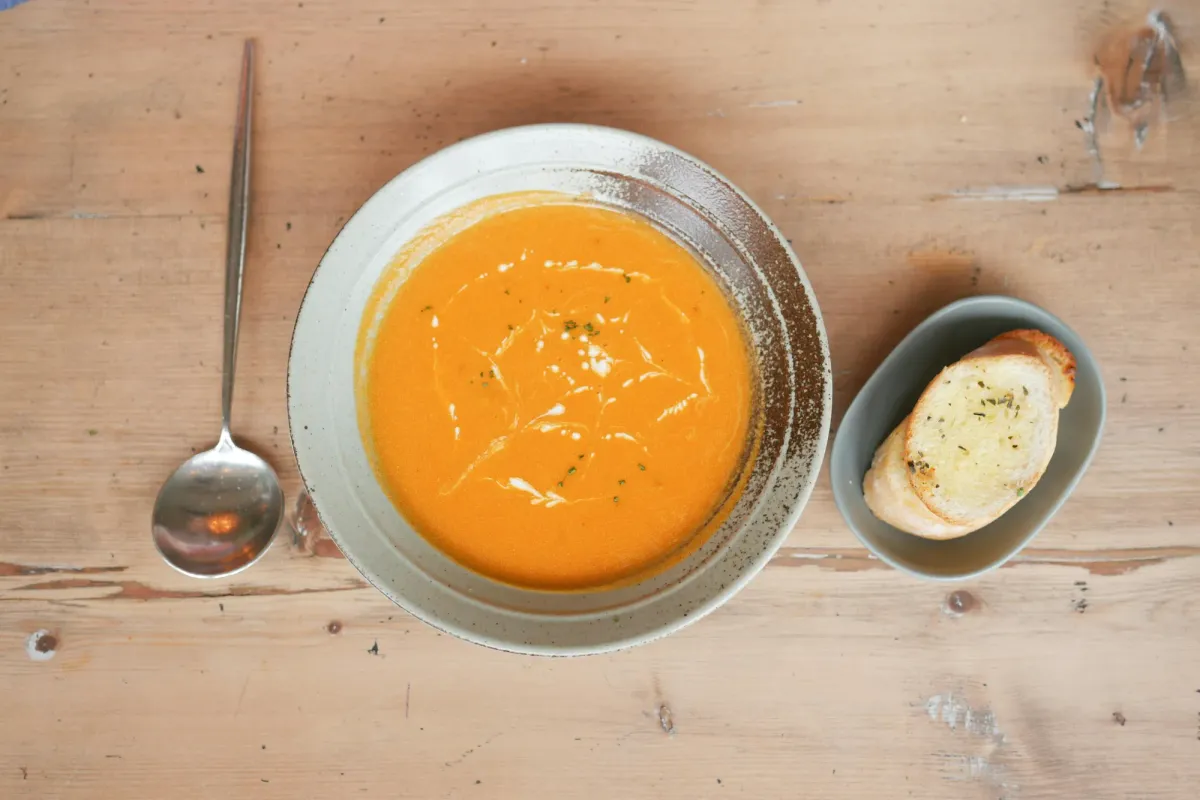 Bowl of soup, a spoon and crusty bread on a wooden table.