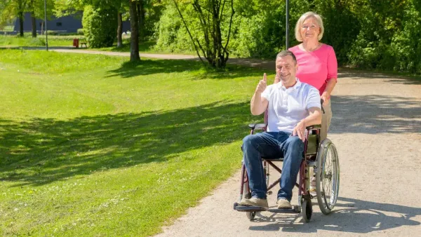 Woman in pink top, pushing man in wheelchair on a country path.