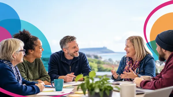 A group of adults having a discussion around a table. Window views of coast.